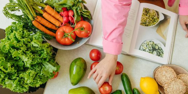 Top view of fresh vegetables and hands arranging them with a recipe book, promoting healthy eating.